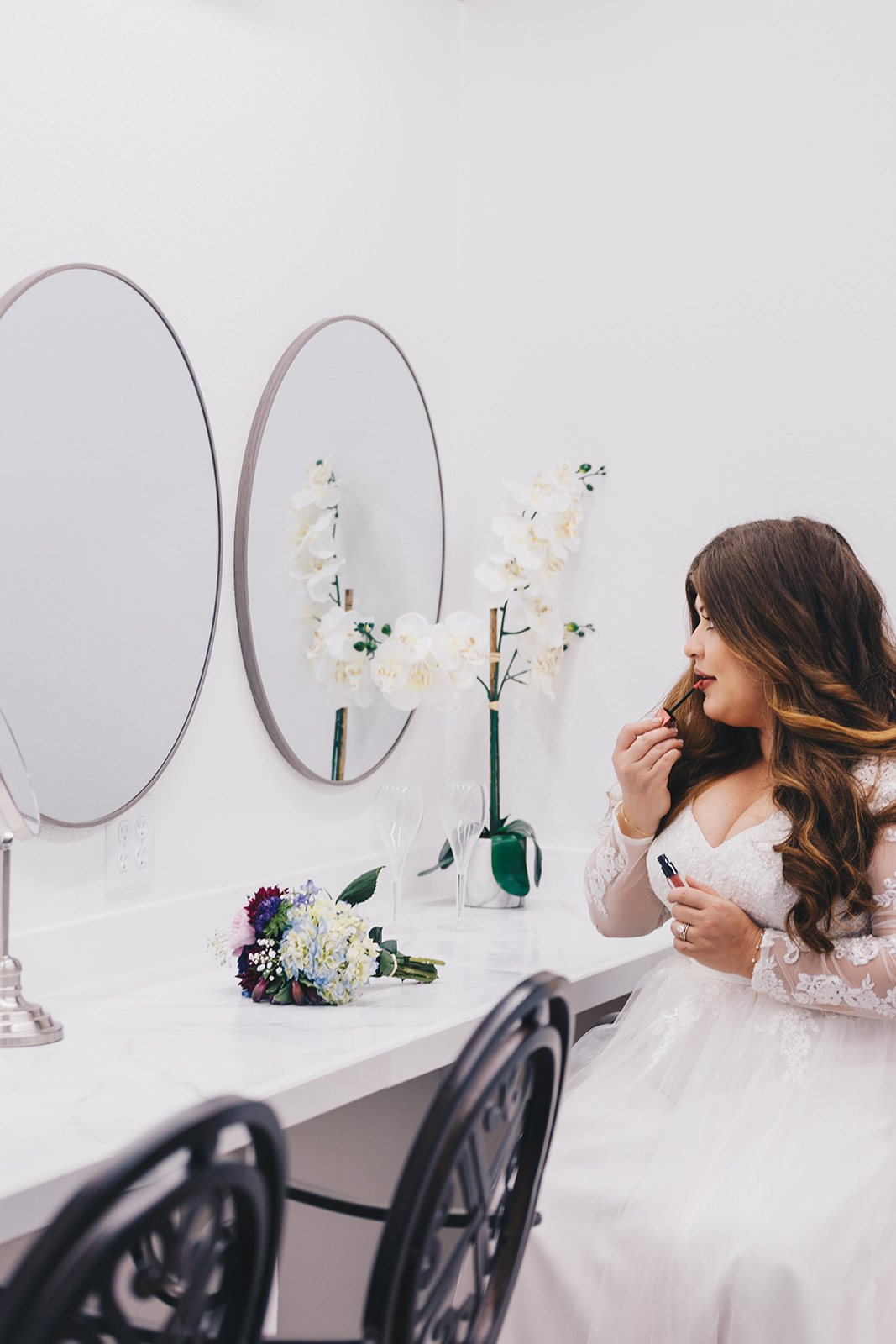 A bride getting ready at the Bridal Suite vanity, with round mirrors and white orchids.