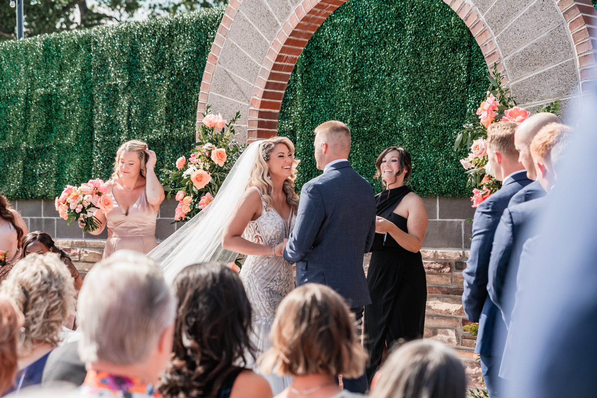 A bride and groom laughing with their officiant under the arch.