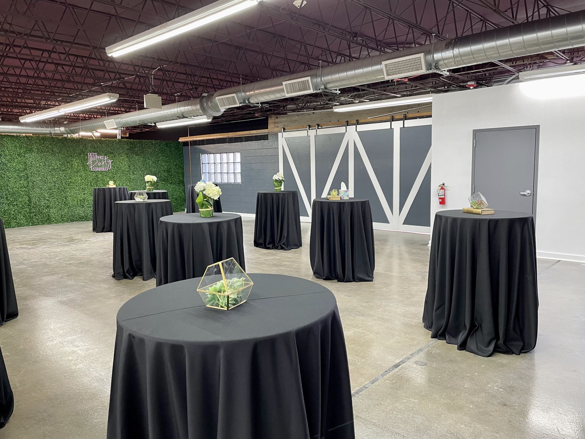 Cocktail tables in black linens by the greenery wall and barn doors.