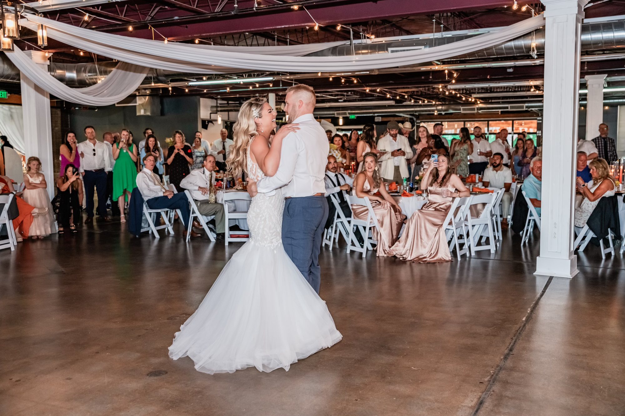 A first dance in the ballroom, guests gathered round under the drapes.