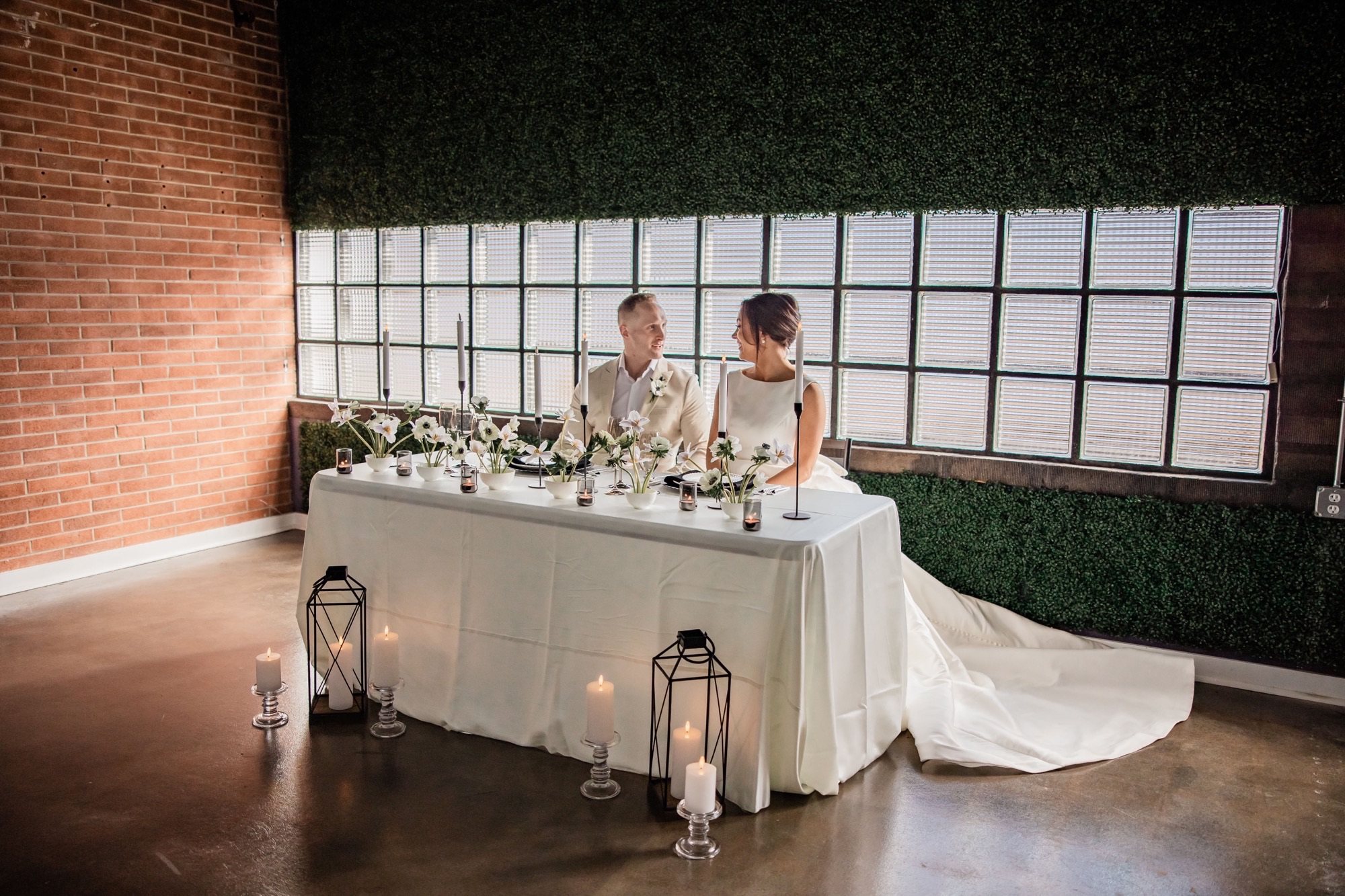 A couple at their sweetheart table by the glass-block windows, with candles and lanterns.