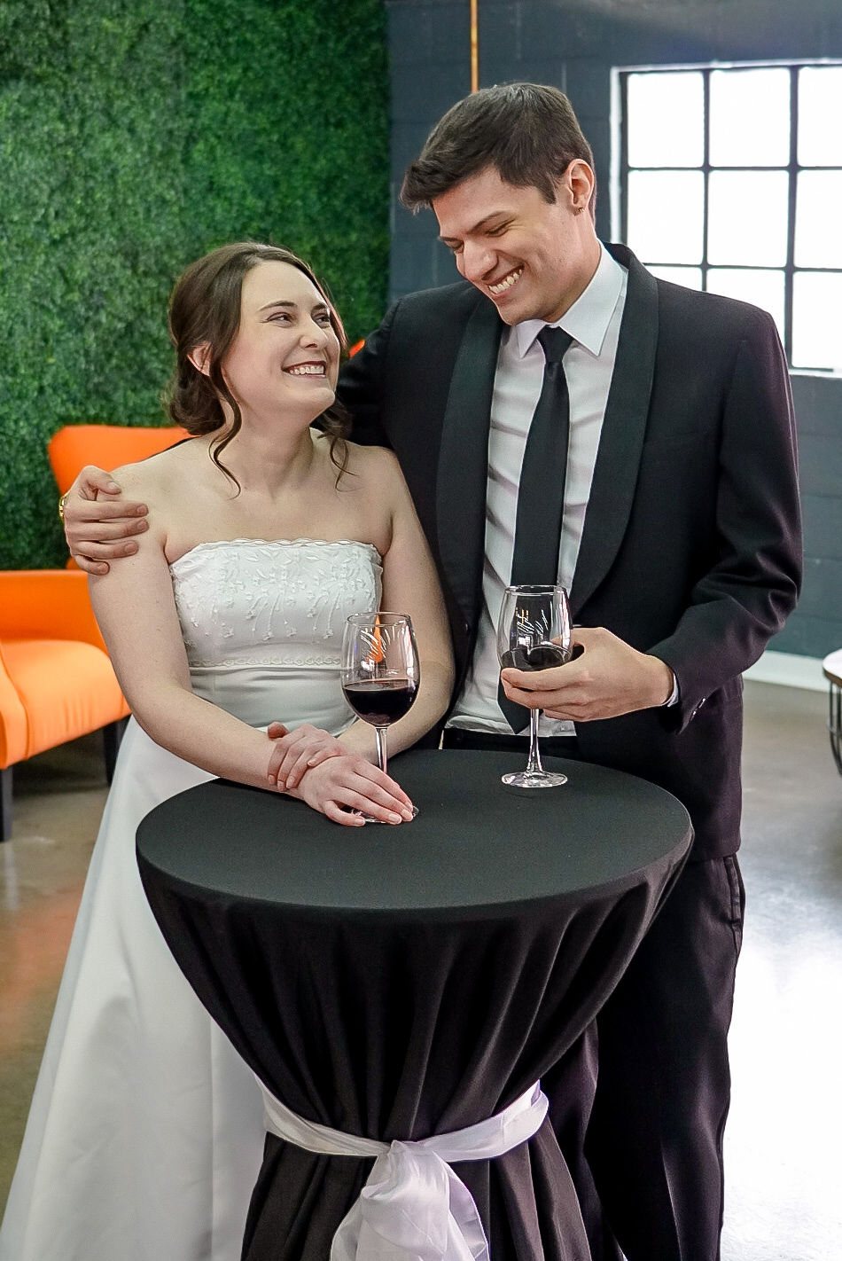 A couple laughing at a cocktail table, an orange armchair behind them.