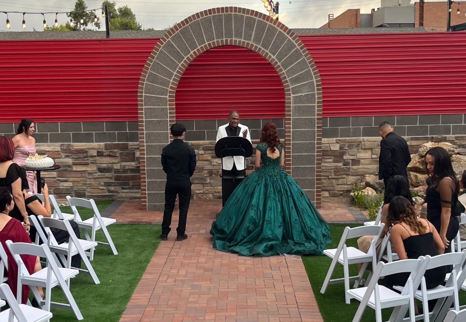 A quinceañera ceremony under the brick arch by the red fence.