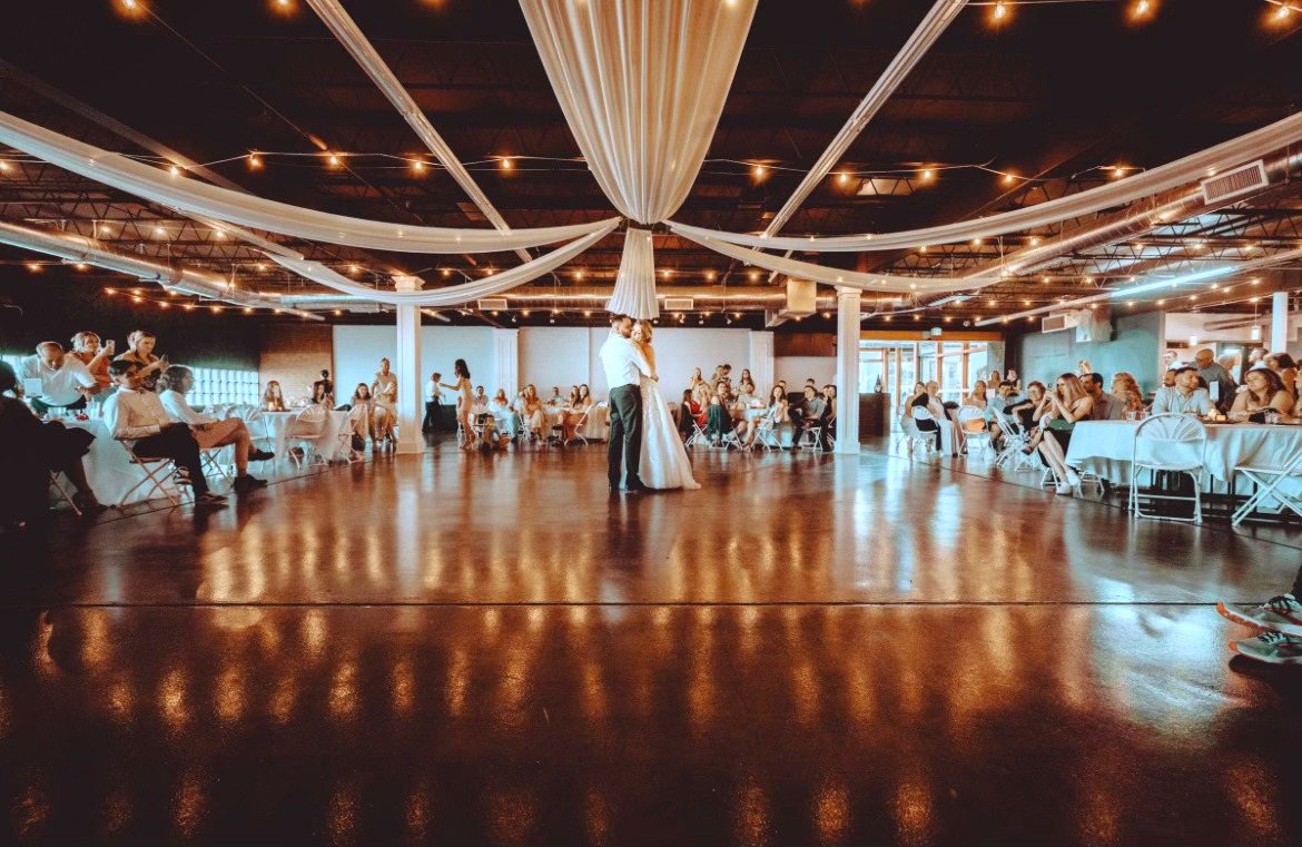 A couple’s first dance under swagged drapes and string lights, guests watching from the tables.