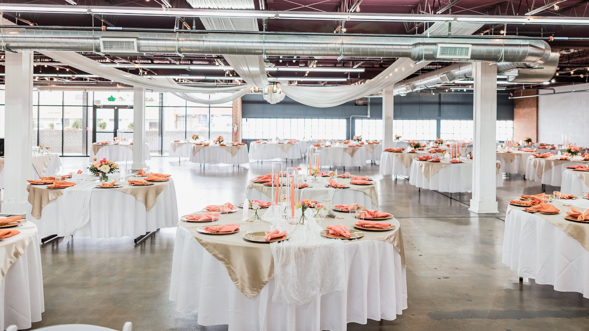 A wide view of a reception room with tables, ceiling drapery and a window wall.
