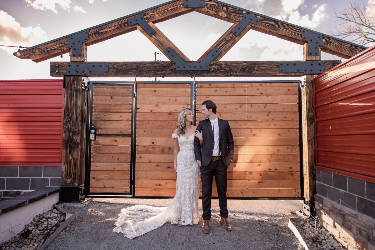 The Redfence Biergarten gate, a timber frame and wooden doors between red fence walls, with a couple in front.